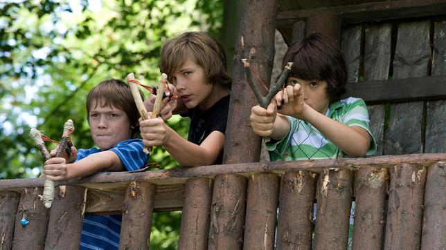 Drei Jungs stehen in ihrem Baumhaus und haben Steinschleudern gespannt zum Abschuss