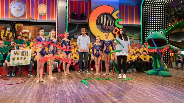 Die Moderatoren Jessica Schöne und Johannes Zenglein beobachten sorgsam die Fingerferigkeit, die das Mitglied des deutschen Nationalteams der Rhythmischen Sportgymnastik am Band zeigt. Da muss Jessica wohl noch ein bisschen üben, genau wie Günther Kastenfrosch.