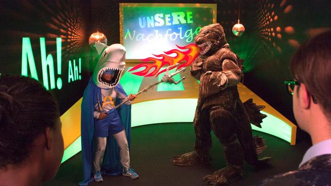 Bild: WDR/Thorsten Schneider Shary und Ralph präsentieren heute in einer Castingshow die Suche nach ihren Nachfolgern. An den Start gehen zwei Moderatoren aus der Zukunft, die Shary und Ralph richtig alt aussehen lassen. Ebenfalls im Rennen sind Sharky und Godzilla (Foto) und die beiden Alternativen Harry und Heike.
