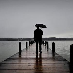 Mann mit Regenschirm steht einsam auf einem Bootssteg