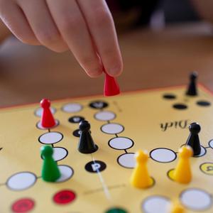 Eine Hand hält eine Spielfigur über dem Spielfeld von "Mensch ärgere dich nicht!"