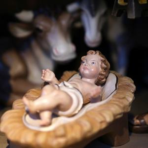 Eine Krippe mit einem Jesuskind, das auf Stroh gebettet ist. Im Hintergrund Schaf, Esel und Kuh.