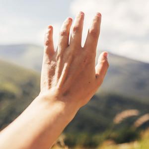 Eine Hand streckt sich nach grünen Hügeln aus