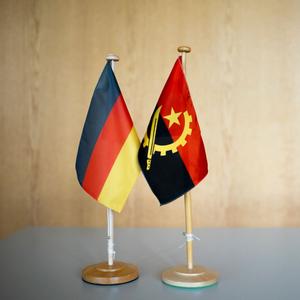 Eine deutsche und eine angolanische Miniatur-Flagge stehen nebeneinander auf einem Tisch.