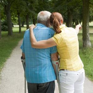 Frau und älterer Mann mit Krücken machen einen Spaziergang im Park