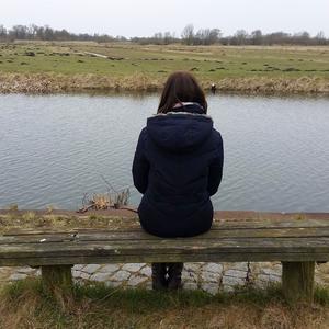 Eine Frau sitzt alleine auf einer Bank vor einem Gewässer-.