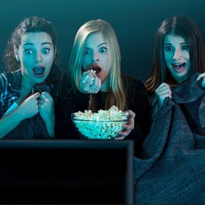 Drei Frauen schauen gespannt, erschrocken auf einen Fernseher.