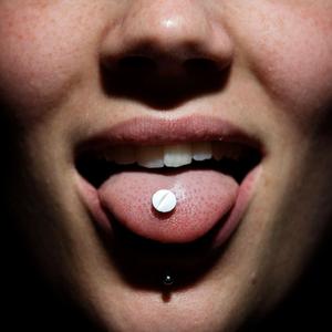 Nahaufnahme eines geöffneten Mundes; auf der Zunge liegt eine weiße Tablette