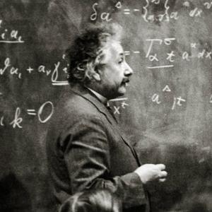 Albert Einstein um 1925. Der Physiker steht vor einer Tafel mit vielen Formeln