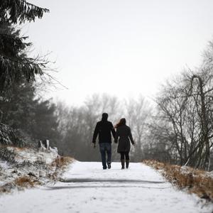 Ein Paar geht Hand in Hand auf einem verschneiten Weg.