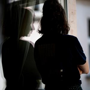  Eine Frau steht mit verschränkten Armen in ihrer Wohnung an einem Fenster