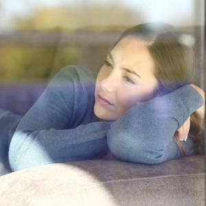 Frau schaut traurig durch ein Fenster: chronisch einsame Menschen sterben früher