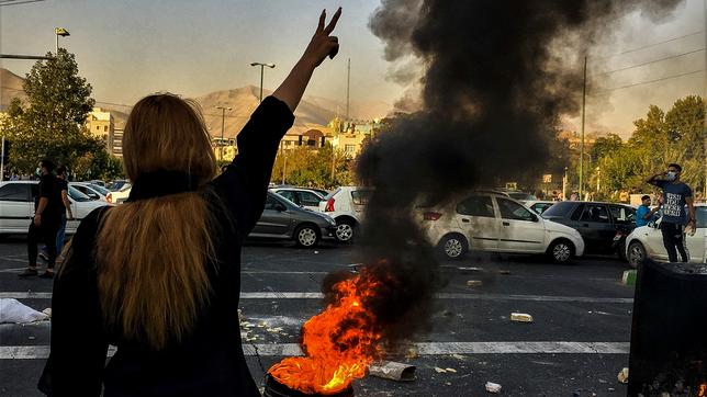 Eine Frau steht während einer Demonstration nach dem Tod der 22-jährigen Mahsa Amini vor einem brennenden Autoreifen und zeigt das Victory-Zeichen. 