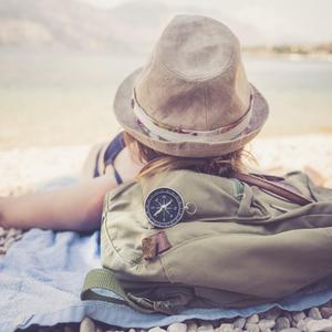 Eine Frau mit Hut und Rucksack liegt entspannt an einem See - Tipps zum Alleinereisen