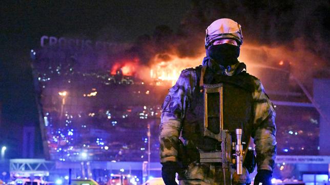 Ein Soldat der russischen Nationalgarde (Rosgwardija) sichert ein Gebiet, während über Crocus City Hall am westlichen Rand Moskaus ein gewaltiger Brand zu sehen ist. 