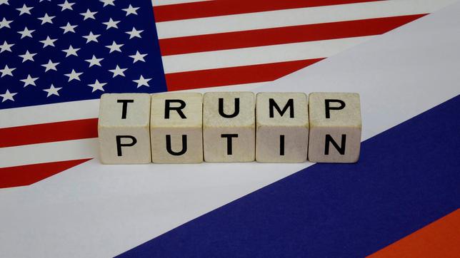 Bild: dpa/Sascha Steinach Auf den Fahnen der USA und Russlands liegen Wuerfel mit den Namen von Trump und Putin.