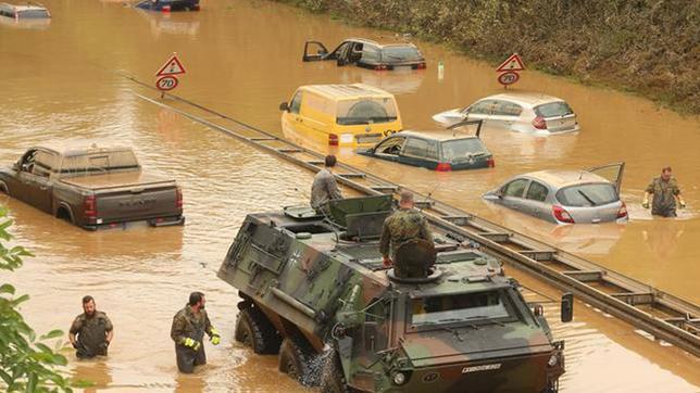 ein Militärfahrzeug und einige PKS stehen auf einer überfluteten Bundesstraße