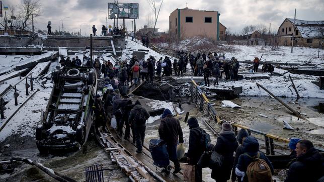Ukrainische Männer und Frauen überqueren auf der Flucht aus Irpin einen behelfsmäßigen Weg zwischen den Trümmern einer zerstörten Brücke.