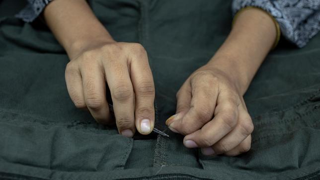 EU-Lieferkettengesetz: Hande, die ein Etikett in ein schwarzes Shirt nähen