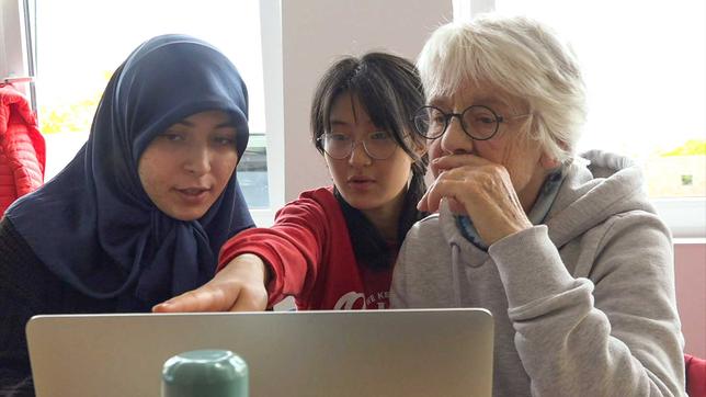 Schülerinnen helfen einer Seniorin am PC