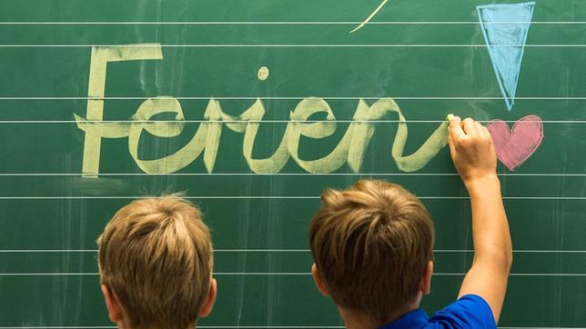 Kinder schreiben "Ferien" an eine Tafel