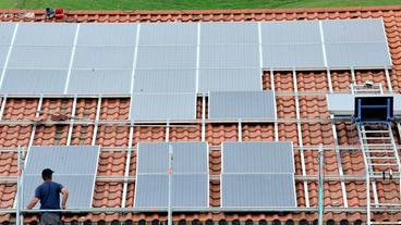 Bild: dpa/Rolf Haid Ein Arbeiter steht auf einem Gerüst vor einem Hausdach um Solarpanel zu installieren.