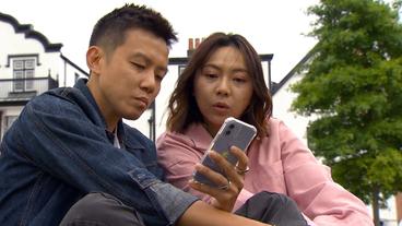 Ein Paar sitzt auf einer Wiese und schaut auf ein Handy.