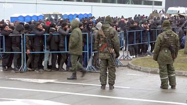 Menschen hinter einer Absperrung, bewacht von Soldaten.