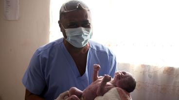 Ein Arzt hält ein Neugeborenes im Arm.