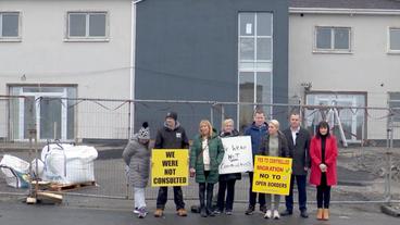 Menschen mit Protestplakaten stehen vor einem Baustelle.