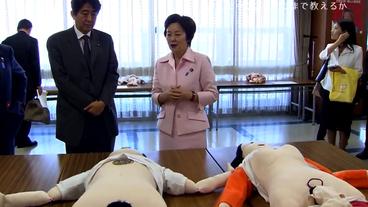 Eriko Yamatani und der heutige Premierminister Abe stehen vor großen Aufklärungspuppen.