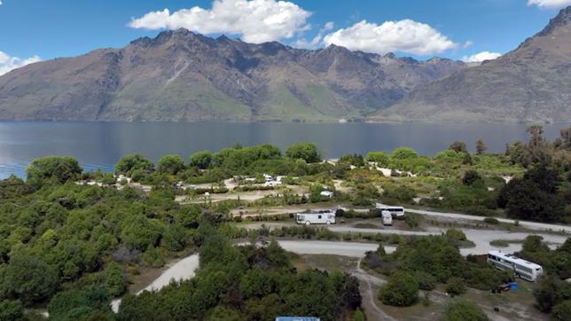 See mit Bergen im Hintergrund und einem Campingstellplatz im Vordergrund.