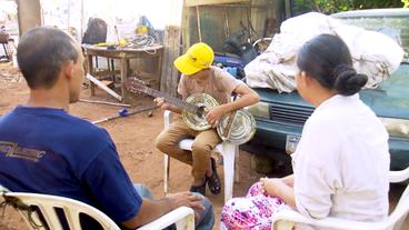 Ein Junge spielt Gitarre, zwei Erwachsene sehen zu.