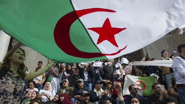 Junge Männer und Frauen protestieren mit einer algerischen Flagge