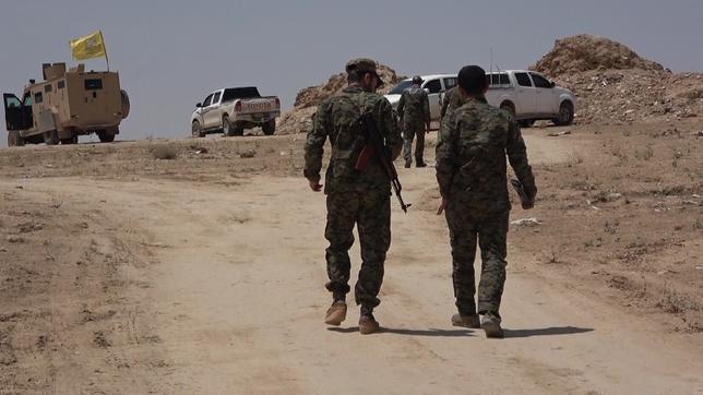 Zwei Soldaten in einer wüstenartigen Landschaft mit Fahrzeugen im Hintergrund