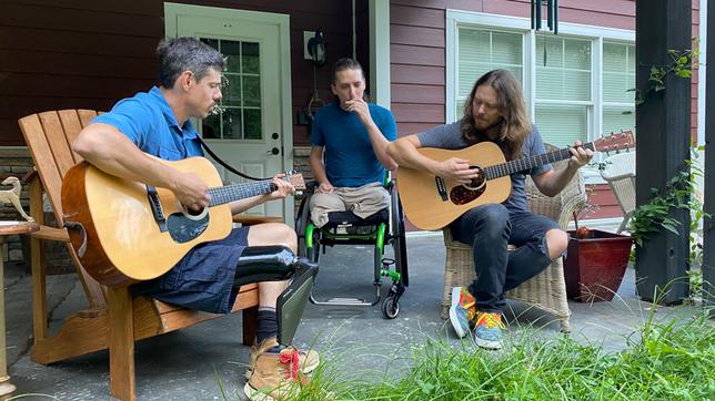 Drei Männer, zwei davon mit Gitarren, einer im Rollstuhl machen Musik.