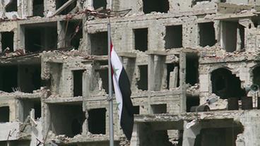 Die syrische Flagge vor zerstörten Häusern