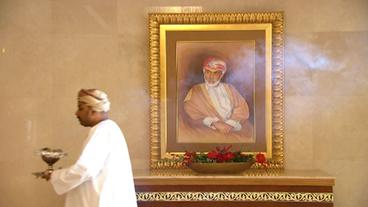 Ein Mann geht mit einer Weihrauchschale vor einem Bild des Sultans vorbei.