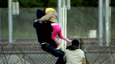 Flüchtlinge klettern über einen Zaun