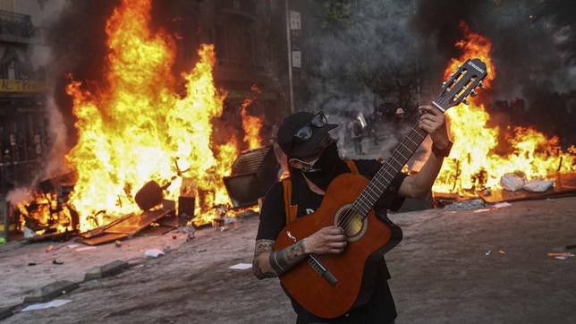 Demonstrant spielt vor einer brennenden Barrikade seine Gitarre