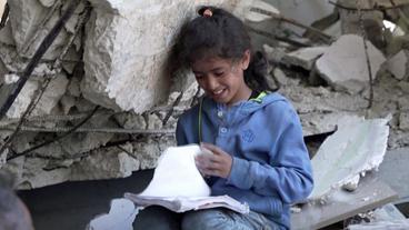 Kind sitzt mit Schulbuch in Trümmern