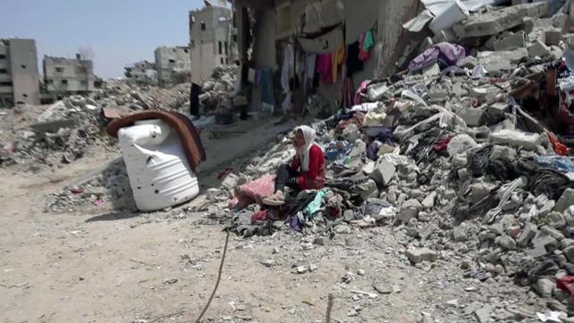 Frau sitzt vor den Trümmern eines Hauses