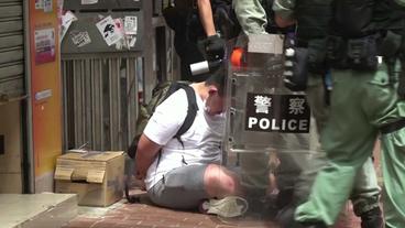 Festgenommener Mann auf dem Boden sitzend umringt von Polizisten