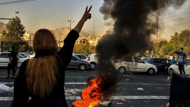 Eine Frau im Iran steht während einer Demonstration vor einem brennenden Autoreifen und zeigt das Victory-Zeichen