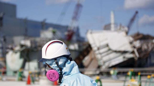 Mann mit Helm und Atemschutz vor zerstörtem Atomkraftwerk in Fukushima