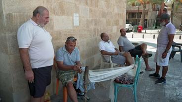 Männer (Fischer) sitzen auf Stühlen, ein Mann repariert ein Fischernetz