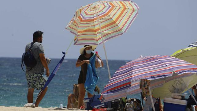 Eine Frau steht mit einer Mund-Nasen-Schutz-Maske am Magaluf-Strand unter einem Sonnenschirm