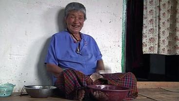 Pelden Dema aus Bhutan sitzt lachend vor ihrem Haus.