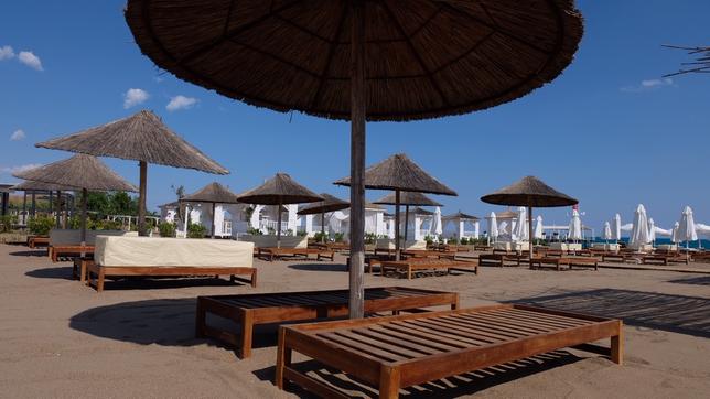 Strandliegen und Sonnenschirme stehen am menschenleeren Strand an einer Hotelanlage.