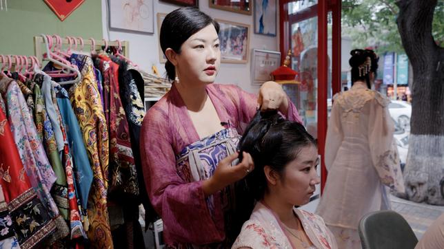 Eine Frau in traditionellen Kleidern in Peking frisiert die Haare einer anderen Frau.